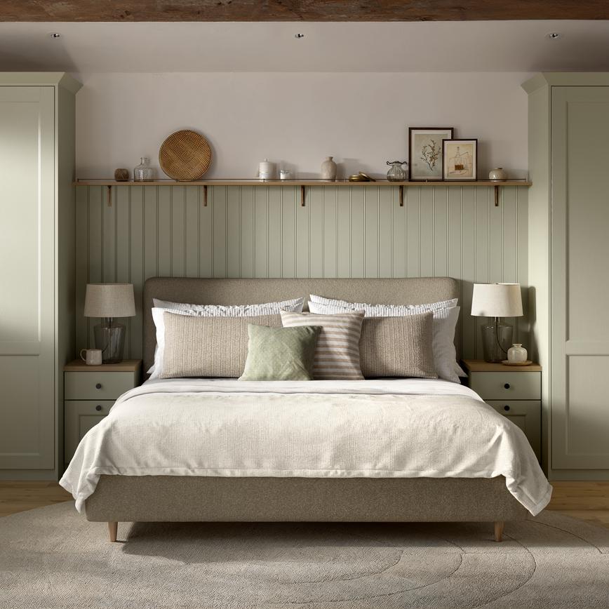 A Bridgemere bedroom with shaker wardrobes in a sage green tone. There is matching, painted wall panels & shelves above.