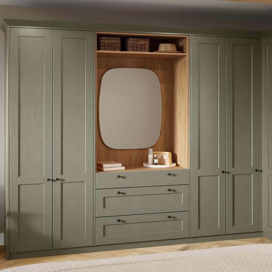 Shaker-style bedroom units in a pale, ash green colour. The tall cabinets feature a desser with drawers and rounded mirror.