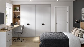 A bedroom with tall, gloss cabinets in a pale, dove grey finish. There is a desk with matching drawers and oak tabletop.
