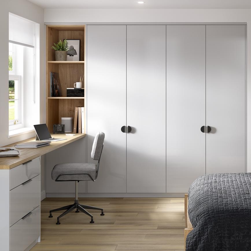 A bedroom with tall, gloss cabinets in a pale, dove grey finish. There is a desk with matching drawers and oak tabletop.