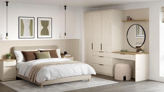 A large bedroom with sandstone cream wardrobe doors in a gloss finish. There is a matching vanity unit with rounded mirror.